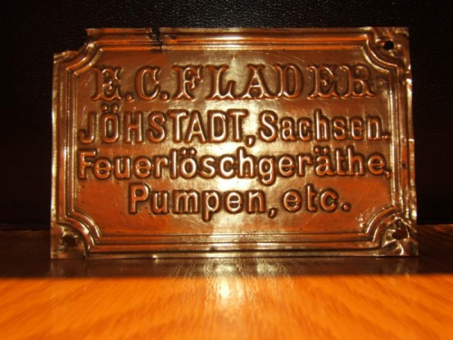 Zdjęcie tabliczki z naszej sikawki konnej. Na tabliczce nazwa firmy: E.C.FLADER, miasto :JOHSTADT, land tj. województwo SACHSEN (Saksonia).
